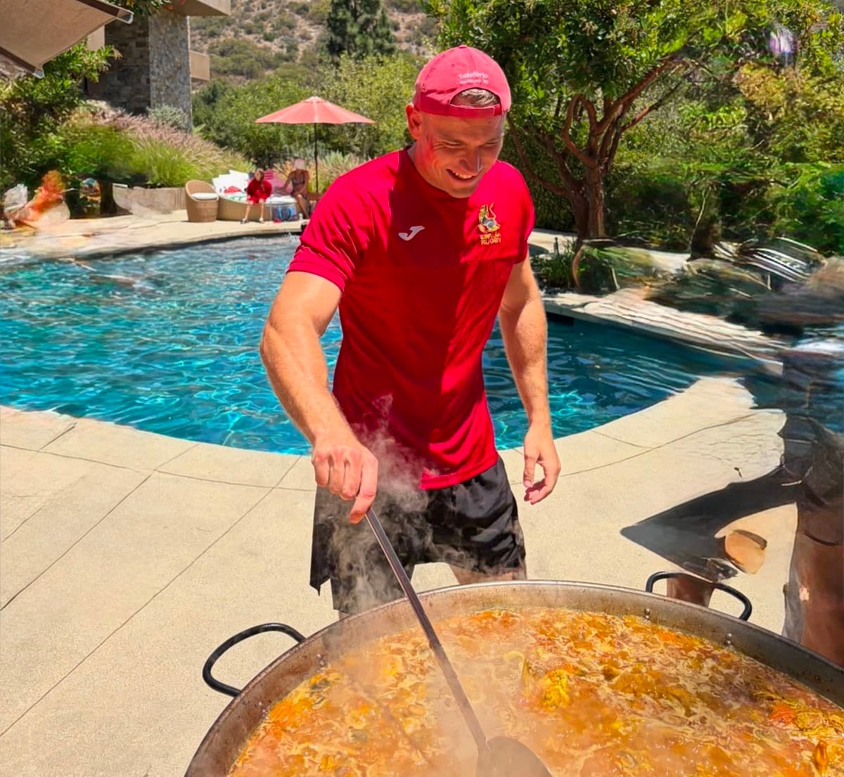 Pau smiling as he stirs a large paella pan by the pool at a private party